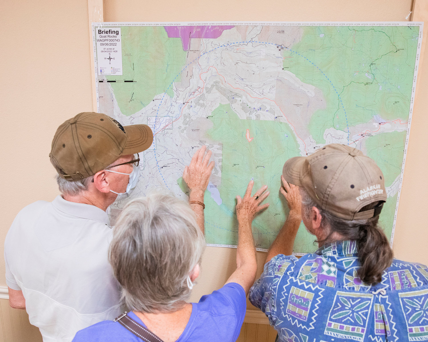 From left, Jim and Patti Correll alongside Greg Arkel, all of Packwood, crowd around a map displaying the Goat Rocks Fire on Tuesday.
