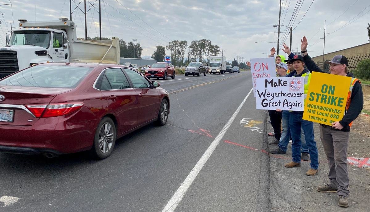 Dylan Cooper, front, Daryn Morris, second to the front, and more Weyerhaeuser woodworkers hold signs and wave Tuesday morning near the intersection of Industrial Way and Washington Way in Longview on the union's first strike day.