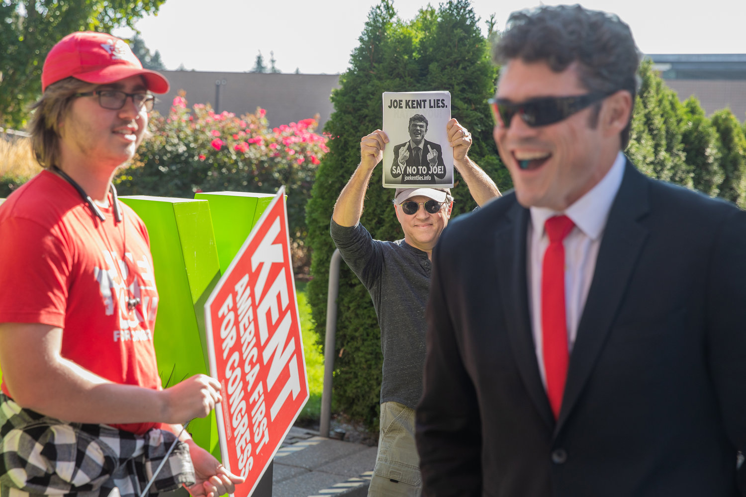 Joe Kent smiles alongside supporters and protesters outside the Vancouver Community Library last month ahead of the Congressional 3rd District Debate.