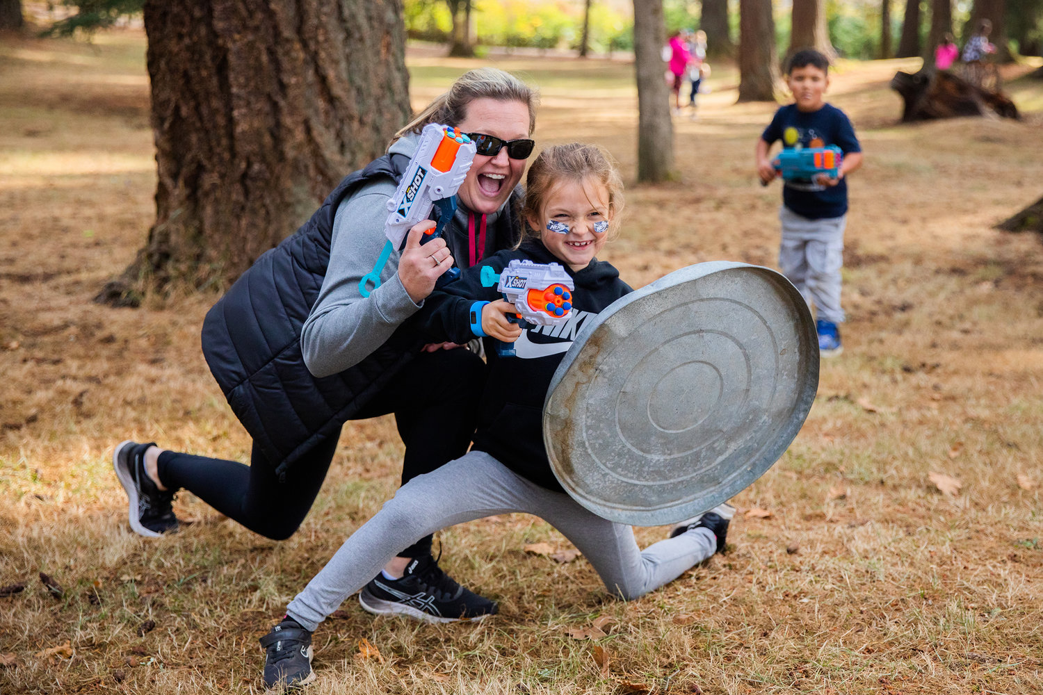 Andra Hankins and Addy, 7, smile for a photo with blasters and a trash can lid shield in hand on Sunday during a Nerf War in honor of Titus Sickles and his Live Life List Fundraiser.