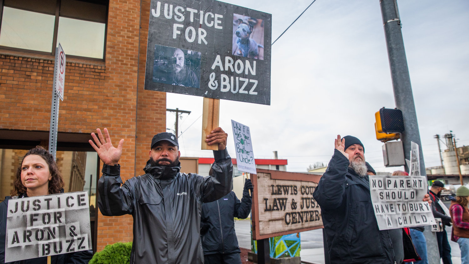 Demonstrators hold signs and wave to honking cars outside the Lewis County Law and Justice Center while demanding justice for Aron Christensen and his dog Buzz in Chehalis on Saturday.