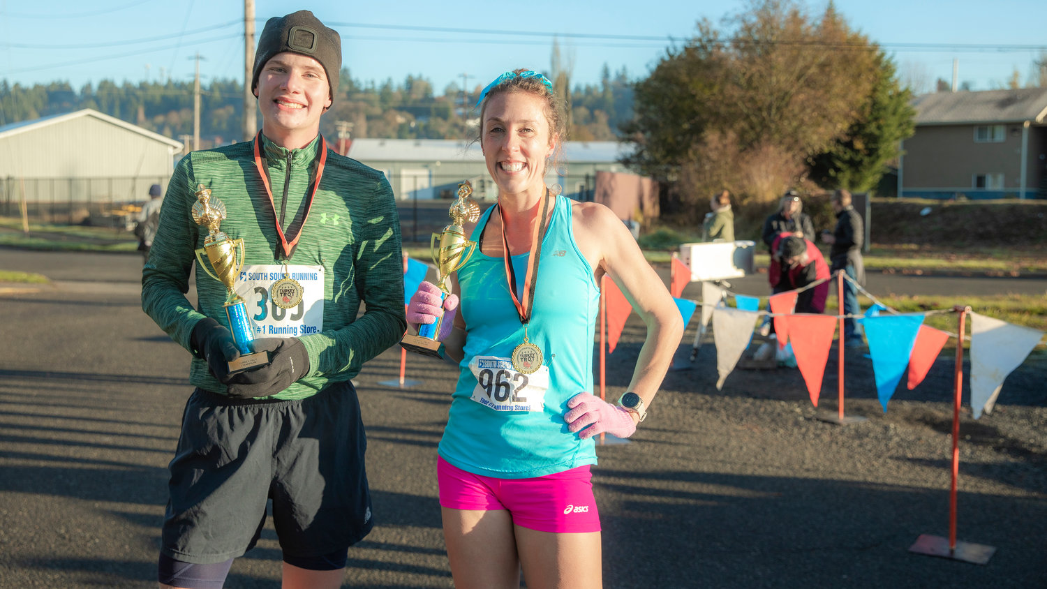 Gunnar Morgan, of Rochester, and Linsie Fisher, of Raymond, smile for a photo with their trophies after being the first two to complete the Turkey Trot 5K Thanksgiving morning outside Thorbeckes in Chehalis.