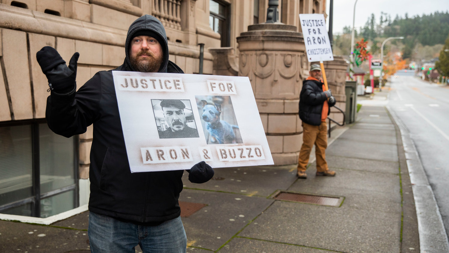 Brian Riedy waves to honking cars outside the Lewis County Courthouse while demanding justice for Aron Christensen and his dog Buzzo in Chehalis on Sunday.