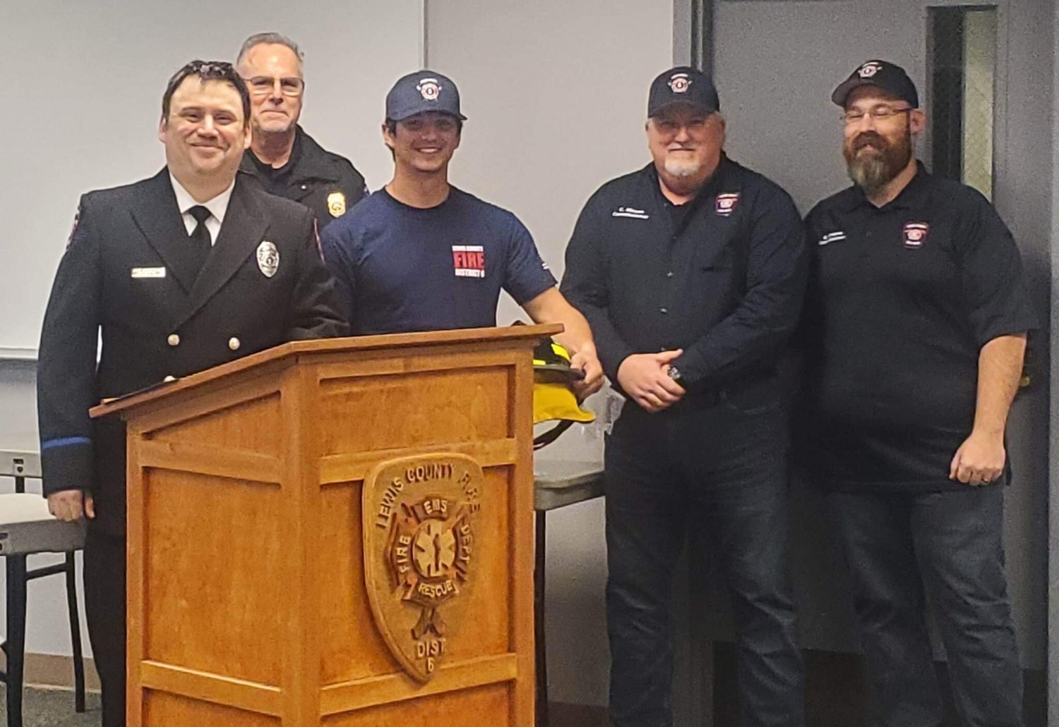 Recruit graduate Trevor Minkoff receiving his certificate, helmet, and challenge coin. (From left to right: Firefighter Mike Goodwillie, Fire Chief Ken Cardinale, Recruit Graduate Trevor Minkoff, Board Chair Colin Mason, and Commissioner Greg Greene)