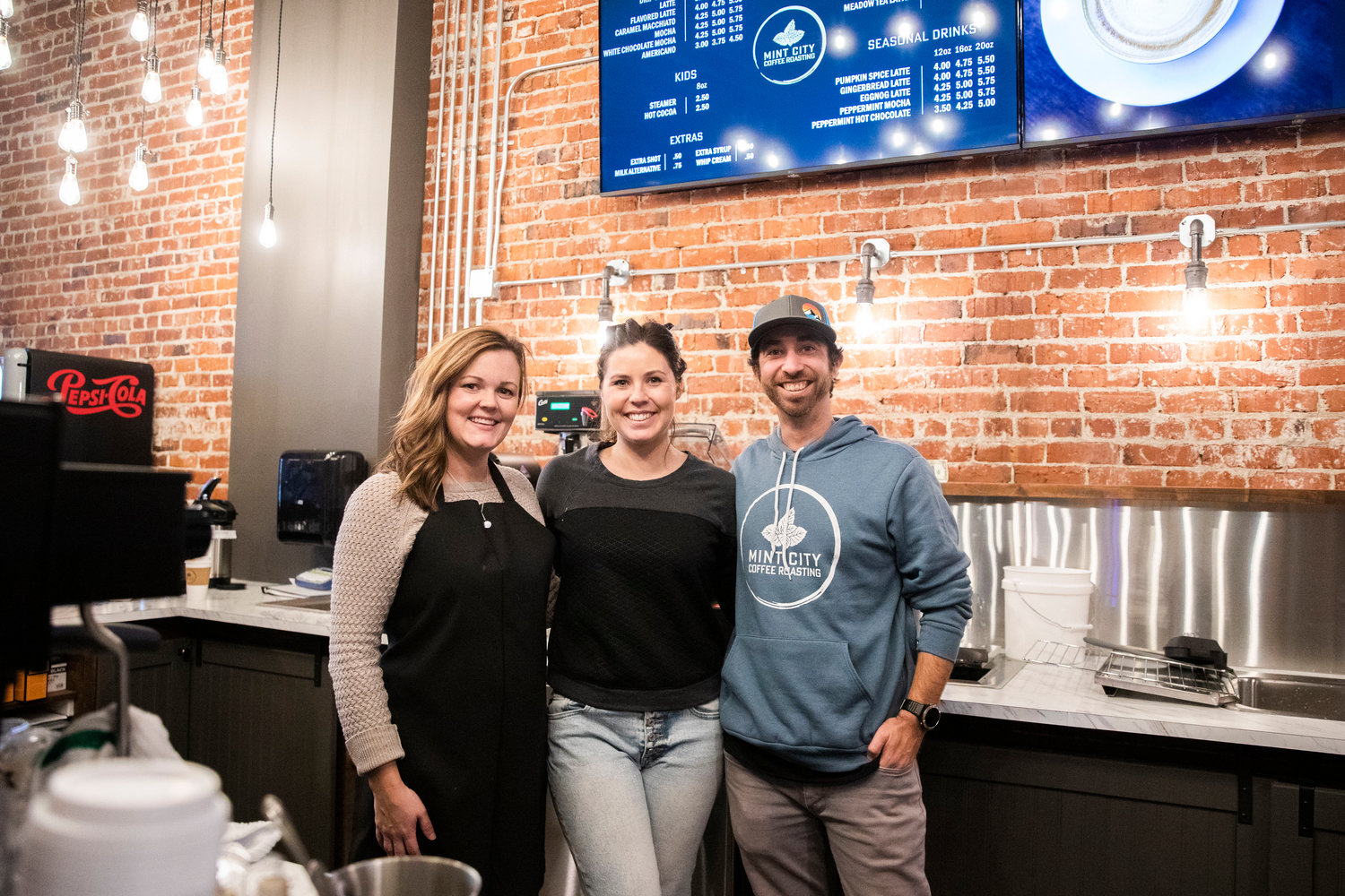 Shawna Boettner smiles for a photo alongside Sarah and Kyle Askin Tuesday morning on opening day at Mint City Coffee Roasting in Chehalis.