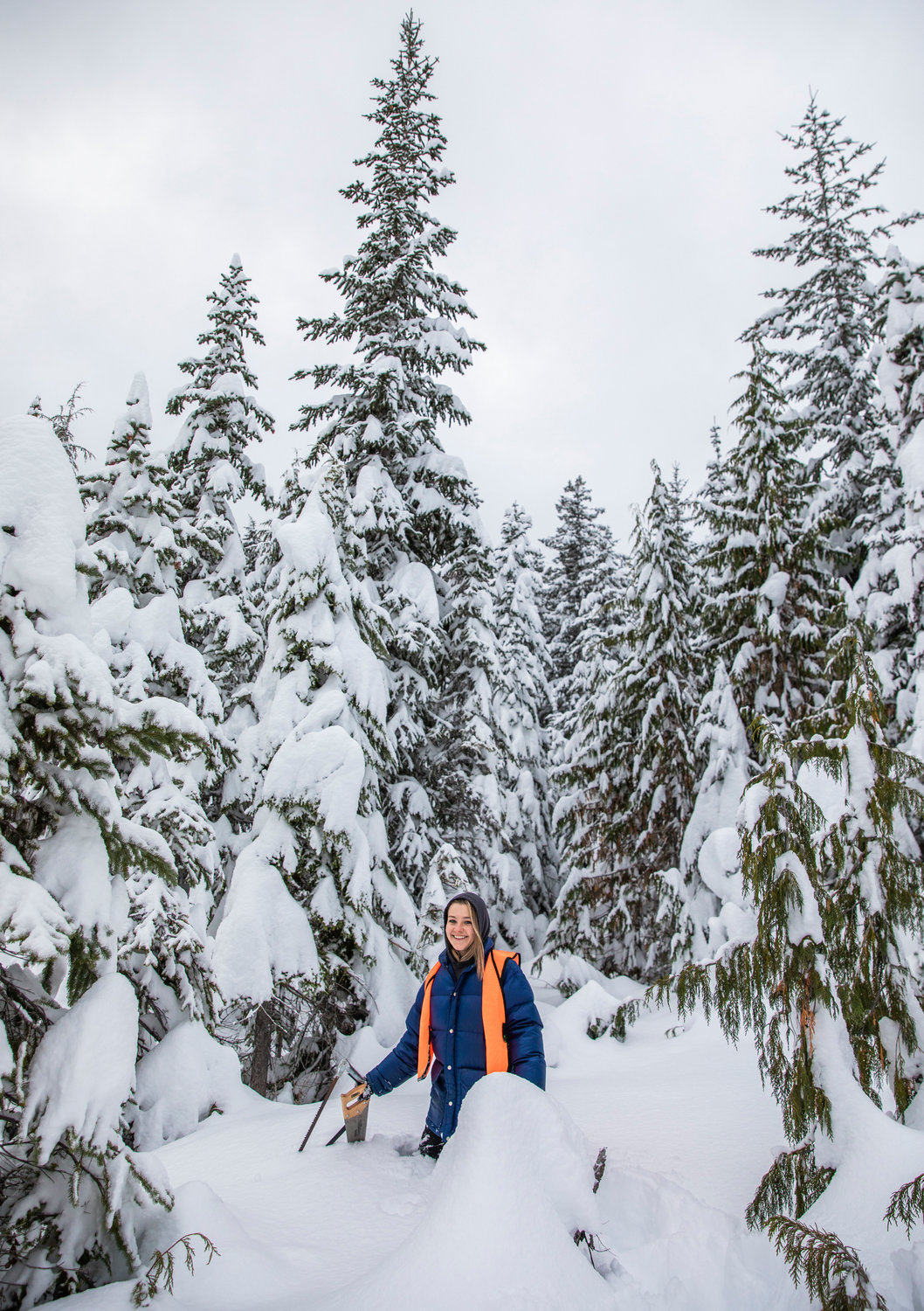 Reporter Isabel Vander Stoep smiles while walking through snow with saws in hand off Forest Road 1284 while looking for a spruce tree to cut down in Lewis County.