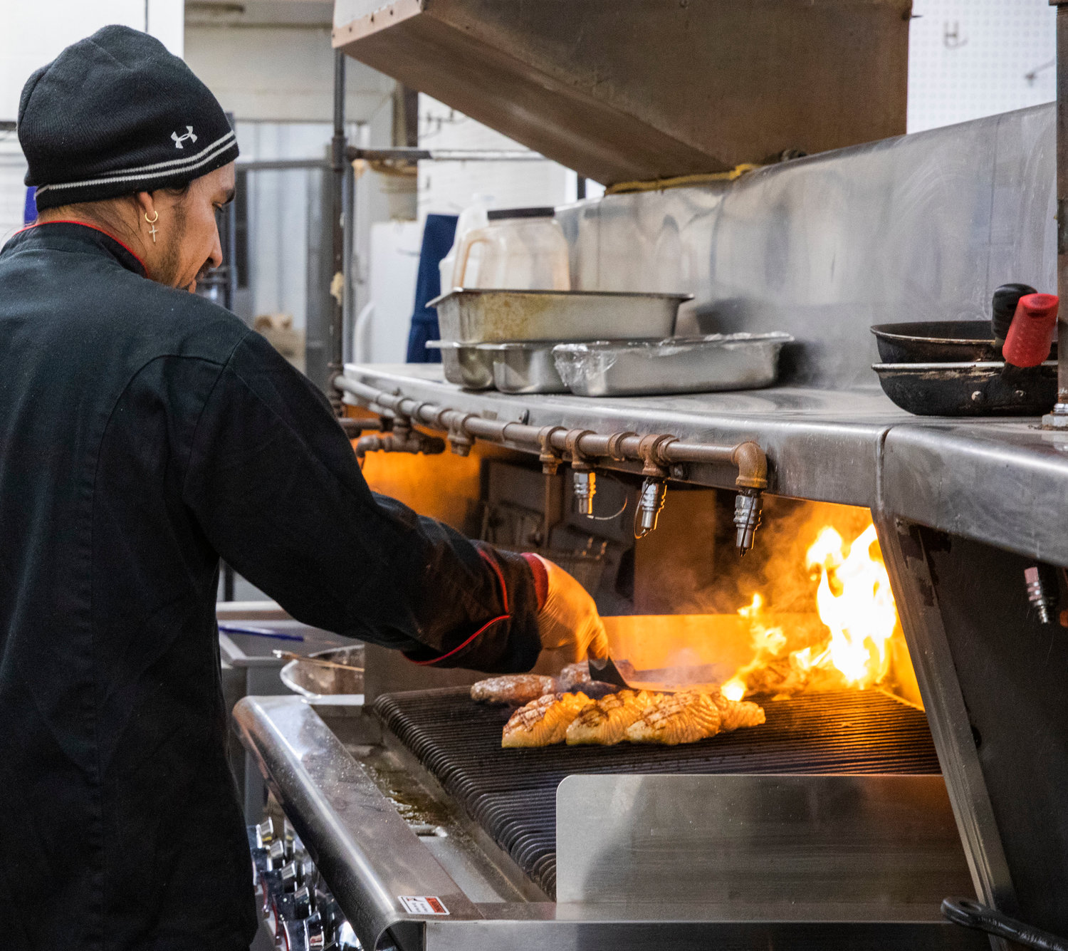 Flames rise from the grill as Owner and Head Chef Eyner Cardona checks burgers and salmon at Ocean Prime Family Restaurant in Chehalis Monday morning.