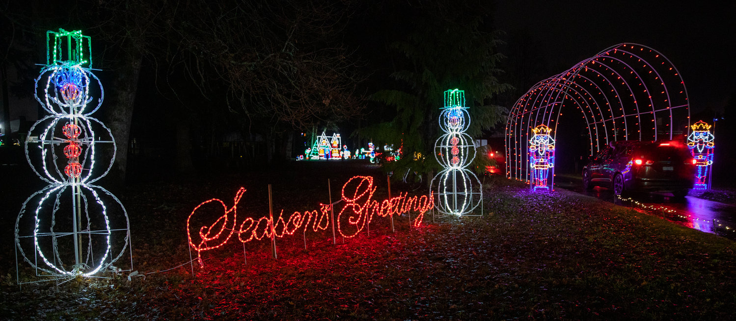 A sign reads, “Season’s Greetings,” as cars drive through a tunnel of Christmas lights illuminating Borst Park Thursday night in Centralia.