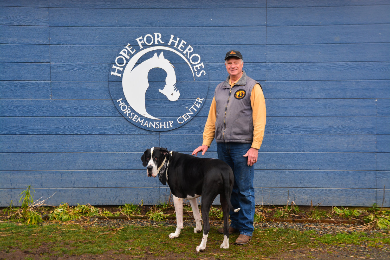 Bob Woelk poses with his dog Junior in front of a Hope for Heroes sign on a tack room.