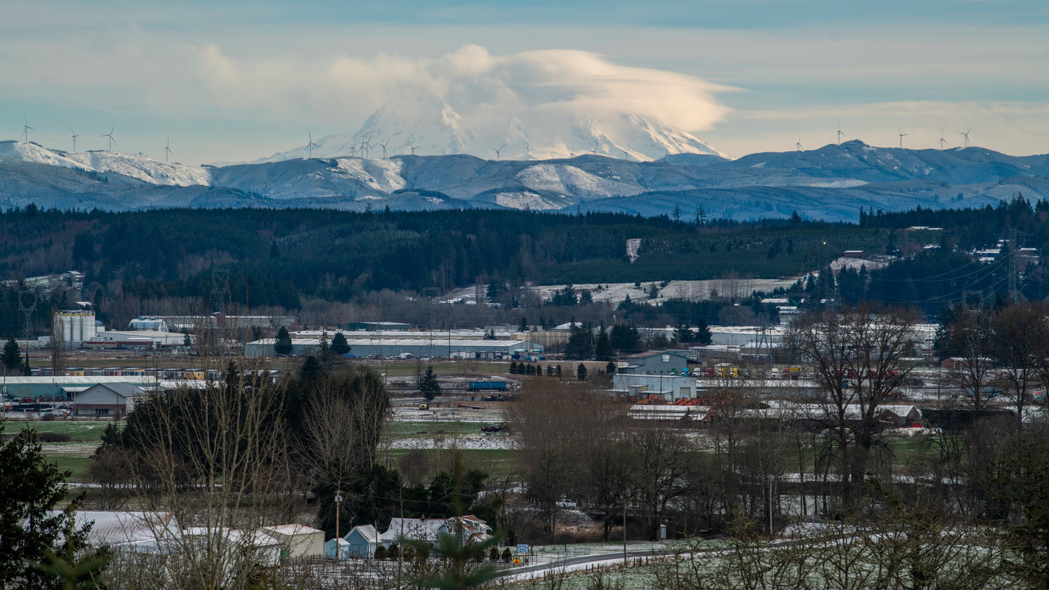 Clouds shroud Mount Rainier as snow sticks to the ground across Lewis County in this photo captured from a vantage point west of Chehalis. Turbines from the Skookumchuck Wind Farm can be seen on the ridge.