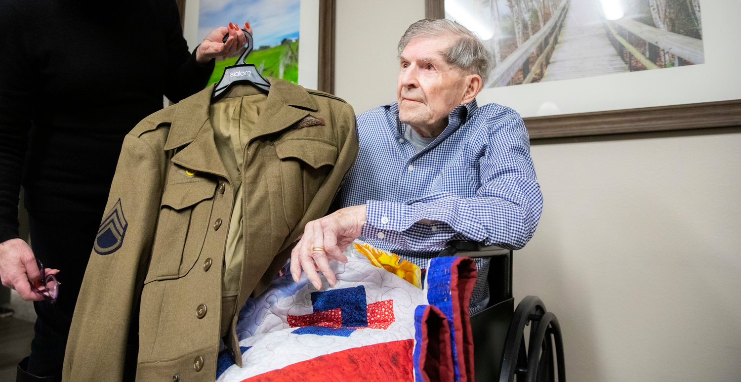 James F. Van Ackeren, a WWII veteran, holds up his U.S. Army coat during a Quilts of Valor ceremony at Woodland Estates in Chehalis on Thursday.