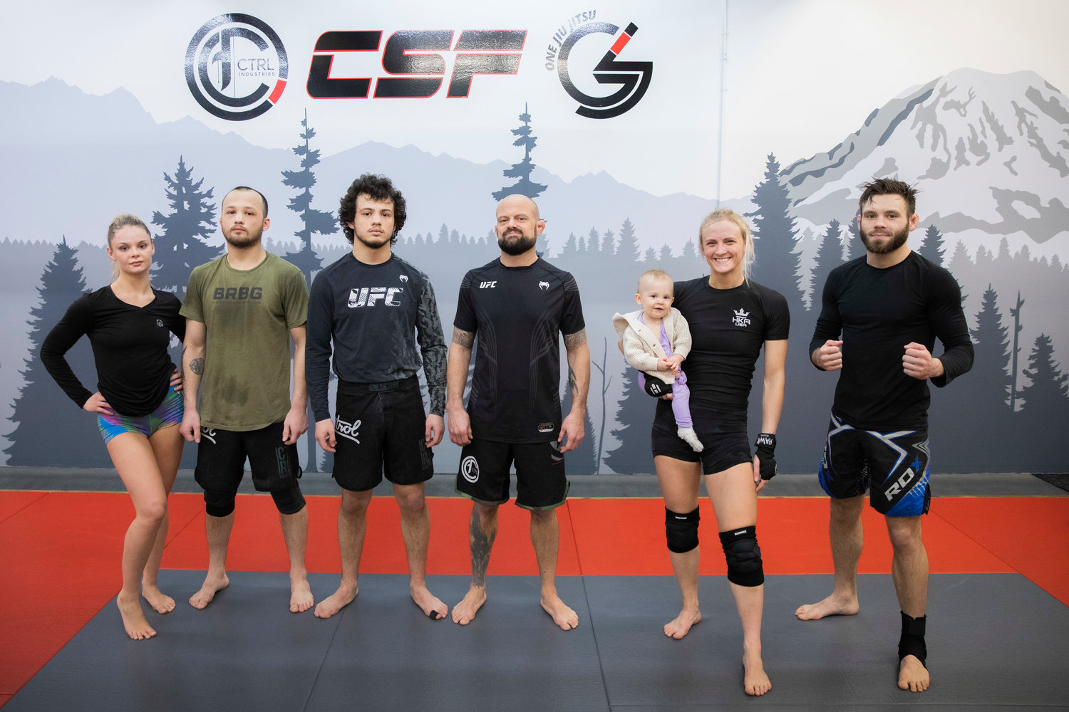 Kayla Weed, a W.F. West graduate, smiles for a photo with her team while holding her 1-year-old daughter Mia inside Combat Sport and Fitness in Enumclaw on Thursday while training for her upcoming fight on March 11, at the Muckleshoot Casino. From left, Caitlyn Williams, Marco and Carlos Martinez, Coach Jeff Hougland, Weed and Landon Taylor.