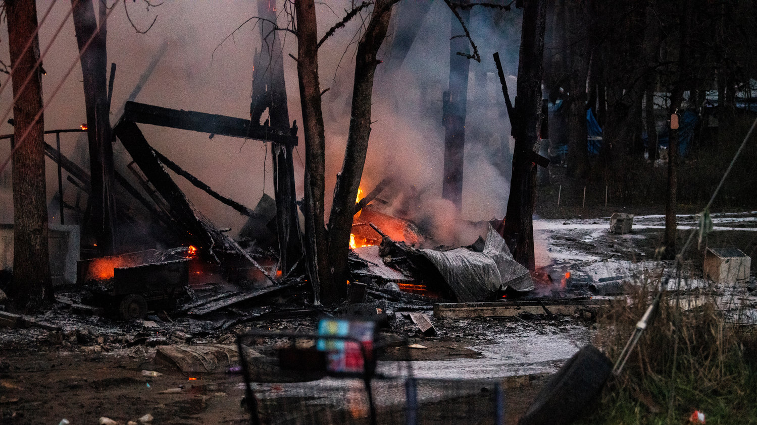 Flames doused in foam ignite debris at the end of Eckerson Road in Centralia near Blakeslee Junction where a column of smoke and heat rose from a structure inside a homeless encampment Tuesday, March 28, 2023.