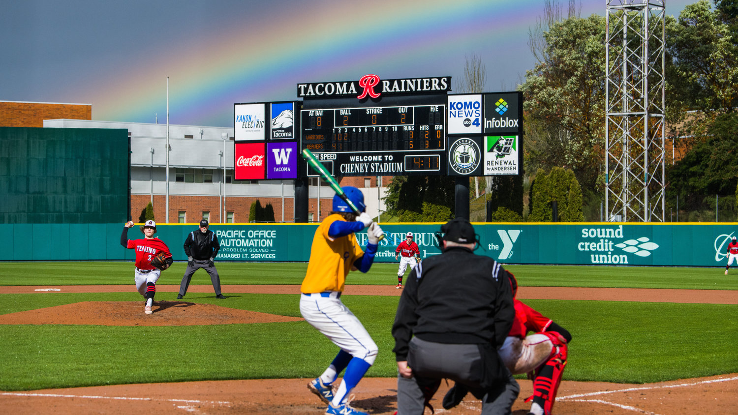 Tenino’s Cody Strawn (2) throws a pitch to Rochester’s Hyde Parrish (8) as a rainbow forms over Cheney Stadium, home of the Tacoma Rainiers, on April 1.