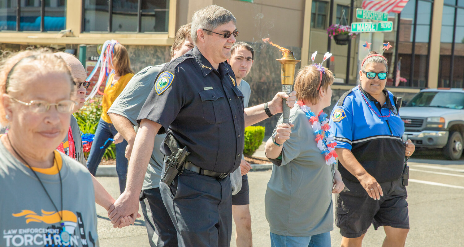 Chehalis Police Chief Randy Kaut holds the torch and a participants hand during the Lewis County Special Olympics Law Enforcement Torch Run on Friday, June 2.