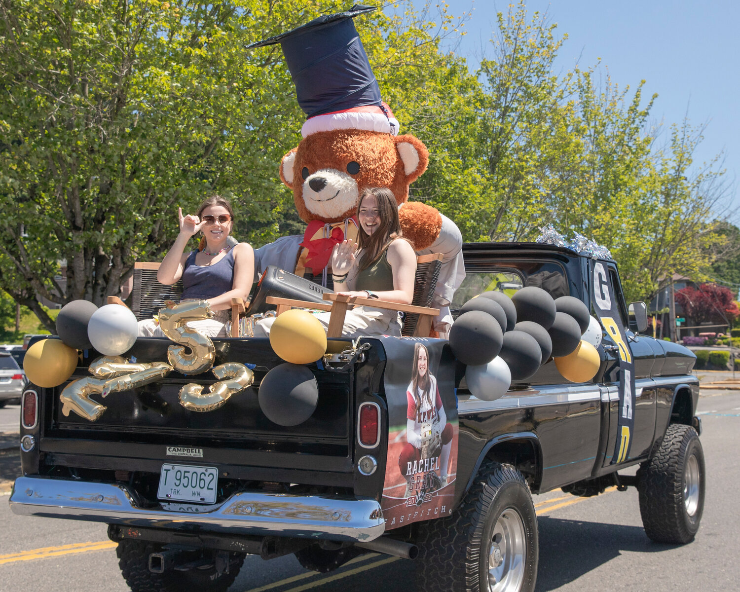 W.F. West High School senior Rachel Gray smiles and waves in front of a giant bear figure sporting a graduation cap during a parade in Chehalis on Sunday, June 4.